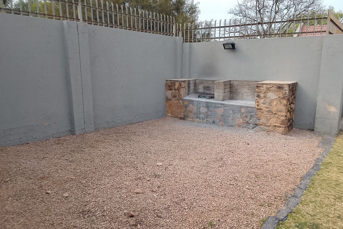 Rear outdoor area featuring a built-in stone-clad braai, gravel ground cover, and high perimeter walls with security spikes.