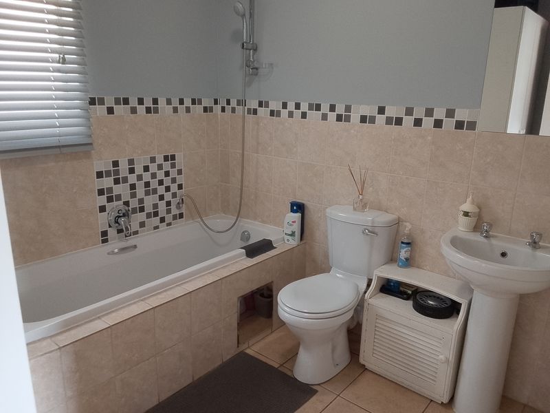 A functional bathroom featuring a bathtub with shower mixer, pedestal basin, and toilet, finished with neutral wall tiles and a decorative mosaic border.
