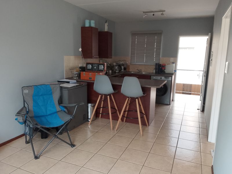 A functional kitchen area featuring laminate countertops, built-in cabinetry, a stainless steel sink, and tiled flooring, with direct access to an outdoor space.