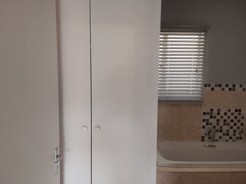 A bathroom featuring a built-in cupboard, a bathtub with a mixer tap, and decorative tiled splashbacks with venetian blinds.
