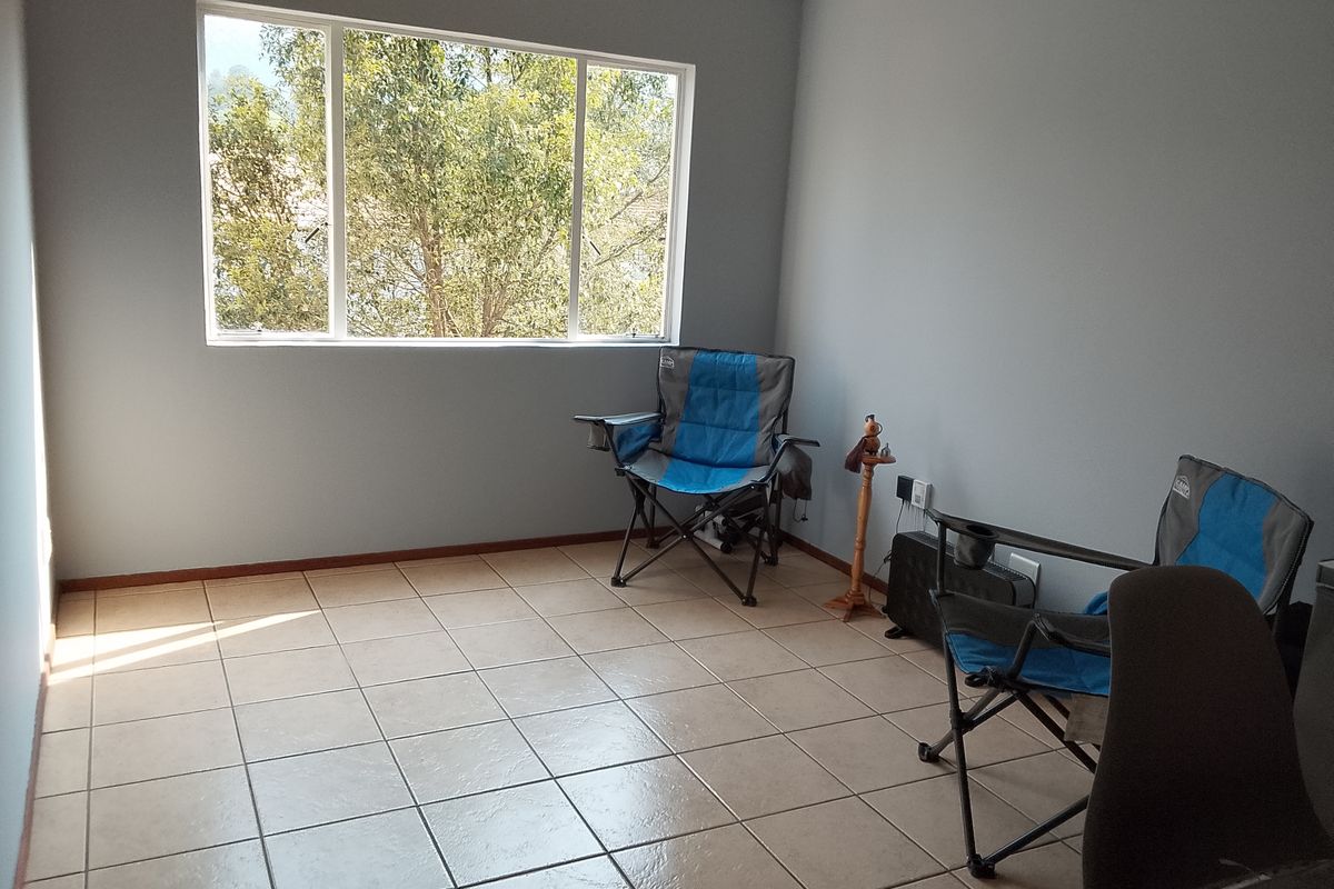 A bright, empty living area featuring neutral tiled flooring and a large window providing natural light and a pleasant outdoor view.