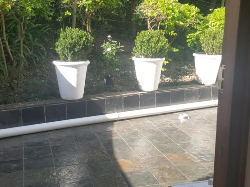 A paved outdoor patio area featuring slate tiles and a low retaining wall, overlooking a garden space.