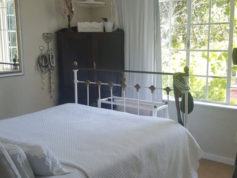 A bedroom featuring a large window with natural light, neutral wall tones, and carpeted flooring.