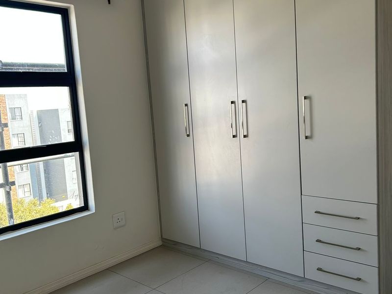 A clean, modern bedroom featuring neutral tiled flooring and ample built-in cupboard storage with a large window providing natural light.