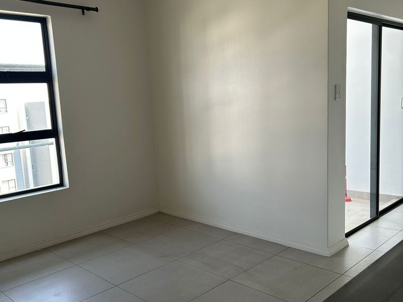 An empty open-plan living area featuring neutral tiled flooring, large windows, and a sliding glass door providing access to an outdoor space.