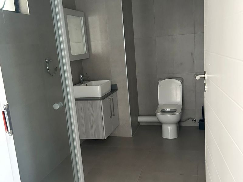 Modern bathroom featuring a glass shower enclosure, wall-mounted vanity with vessel sink, and neutral grey floor-to-ceiling tiling.