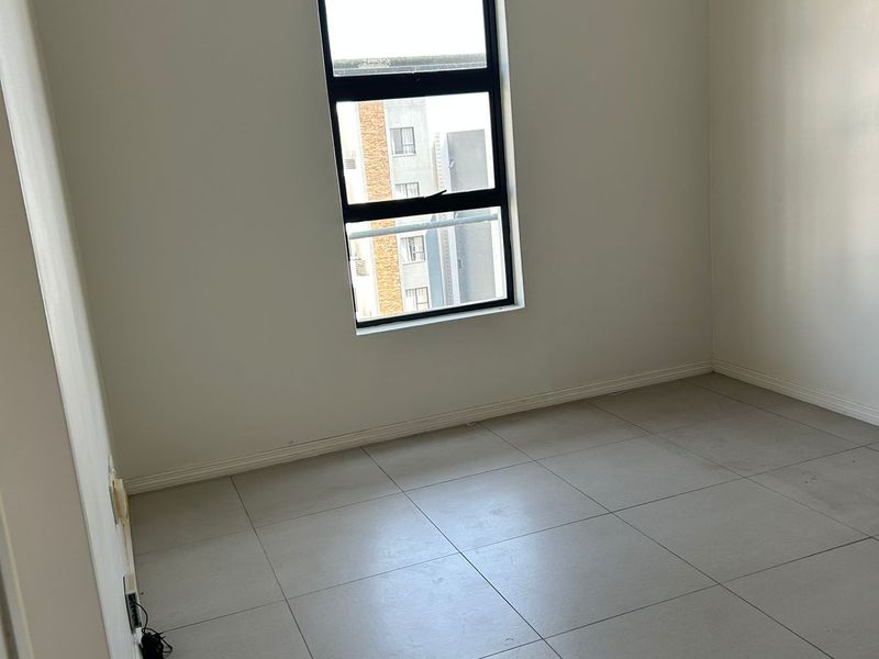 An empty bedroom featuring neutral tiled flooring, white walls, and an aluminium-framed window with a fitted curtain rod.