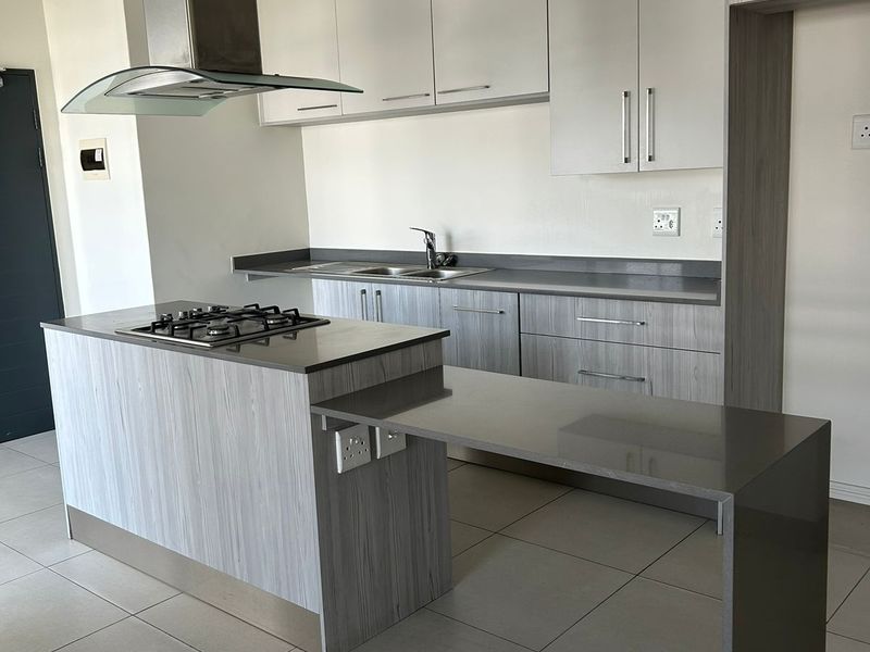 Modern kitchen featuring light wood-grain cabinetry, stone countertops, a central island with a gas hob, and a breakfast bar extension.