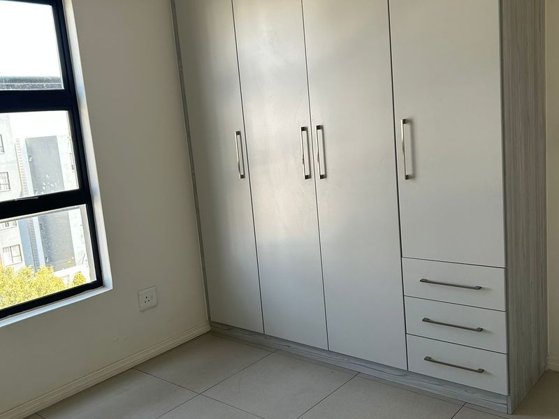 A bright, empty bedroom featuring neutral tiled flooring and a modern, full-height built-in wardrobe with integrated drawers.