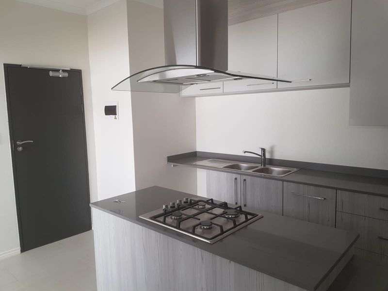 Modern kitchen featuring a central island with a gas hob, stainless steel extractor fan, double sink, and contemporary grey cabinetry with stone countertops.