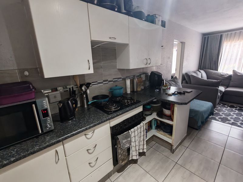 Open-plan kitchen featuring built-in cabinetry, gas hob, and oven, flowing into a living area with tiled flooring throughout.