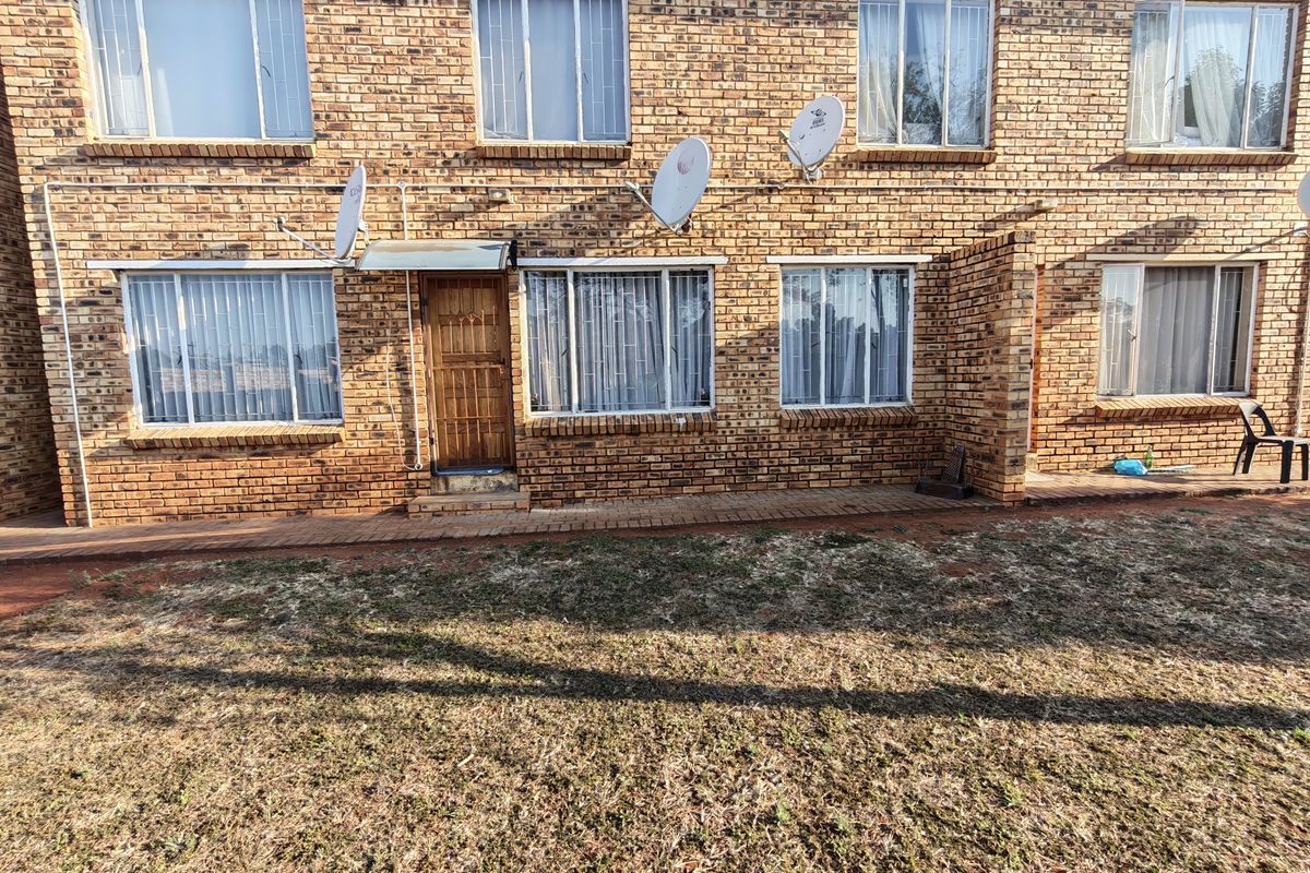 Rear view of a multi-story face brick residential building featuring security gates, window burglar bars, and a paved walkway leading to the lawn.