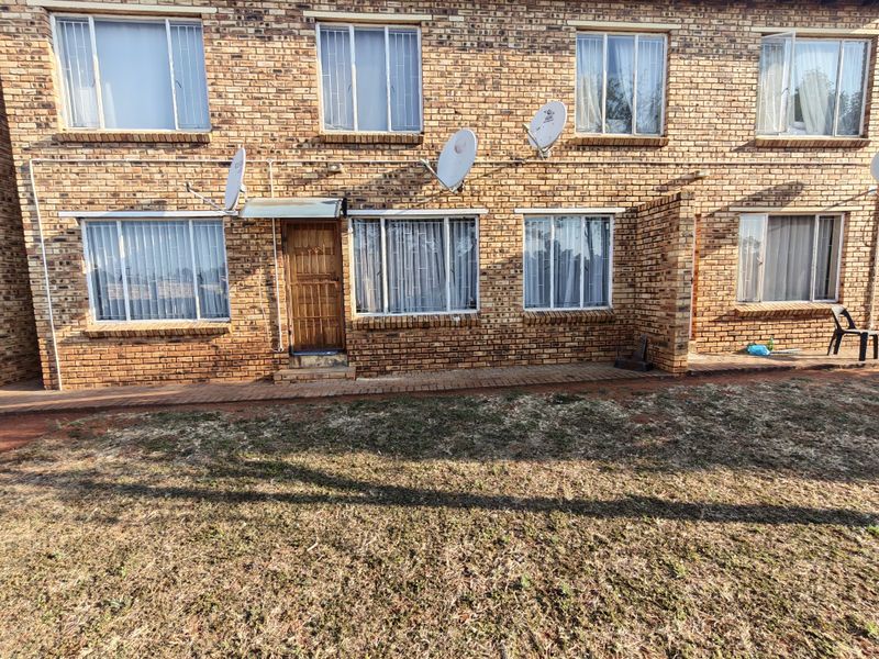 Rear view of a multi-story face brick residential building featuring security gates, window burglar bars, and a paved walkway leading to the lawn.