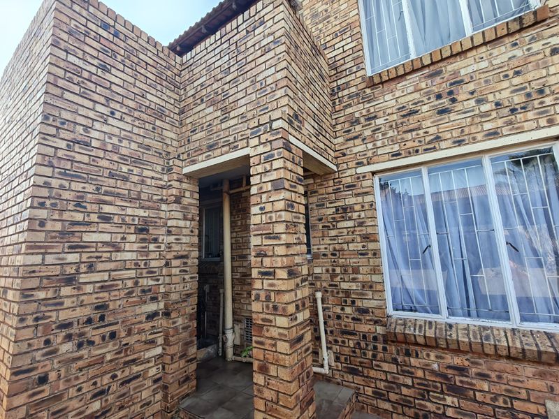 A view of the face brick exterior facade featuring a covered entrance porch and windows fitted with security bars.