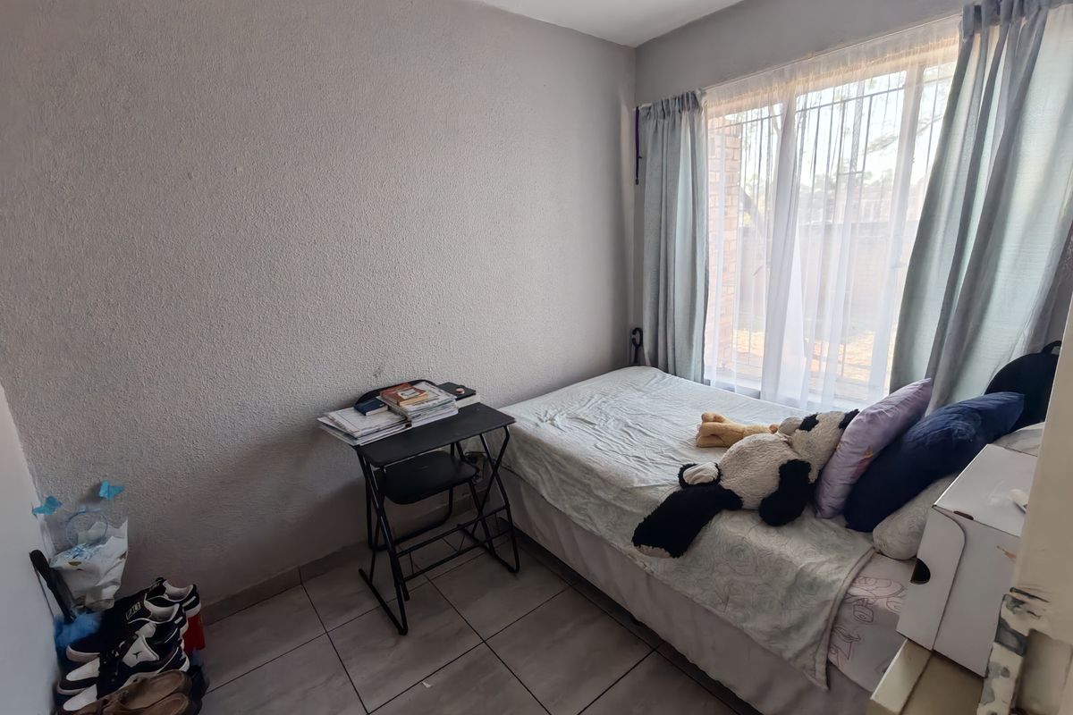 A compact bedroom featuring tiled flooring and a window fitted with security bars, providing natural light.