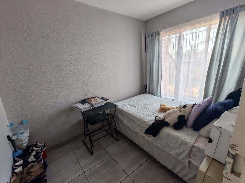 A compact bedroom featuring tiled flooring and a window fitted with security bars, providing natural light.