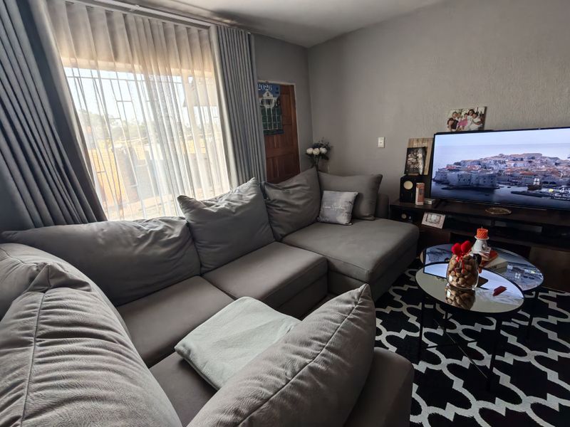A comfortable living room featuring large windows with security bars and neutral wall finishes, providing a functional and well-lit space.