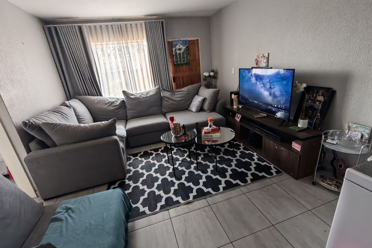 A comfortable living room featuring tiled flooring and large windows with curtain tracks, providing a functional and well-lit space for relaxation.