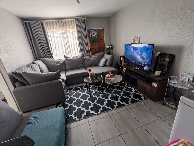 A comfortable living room featuring tiled flooring and large windows with curtain tracks, providing a functional and well-lit space for relaxation.