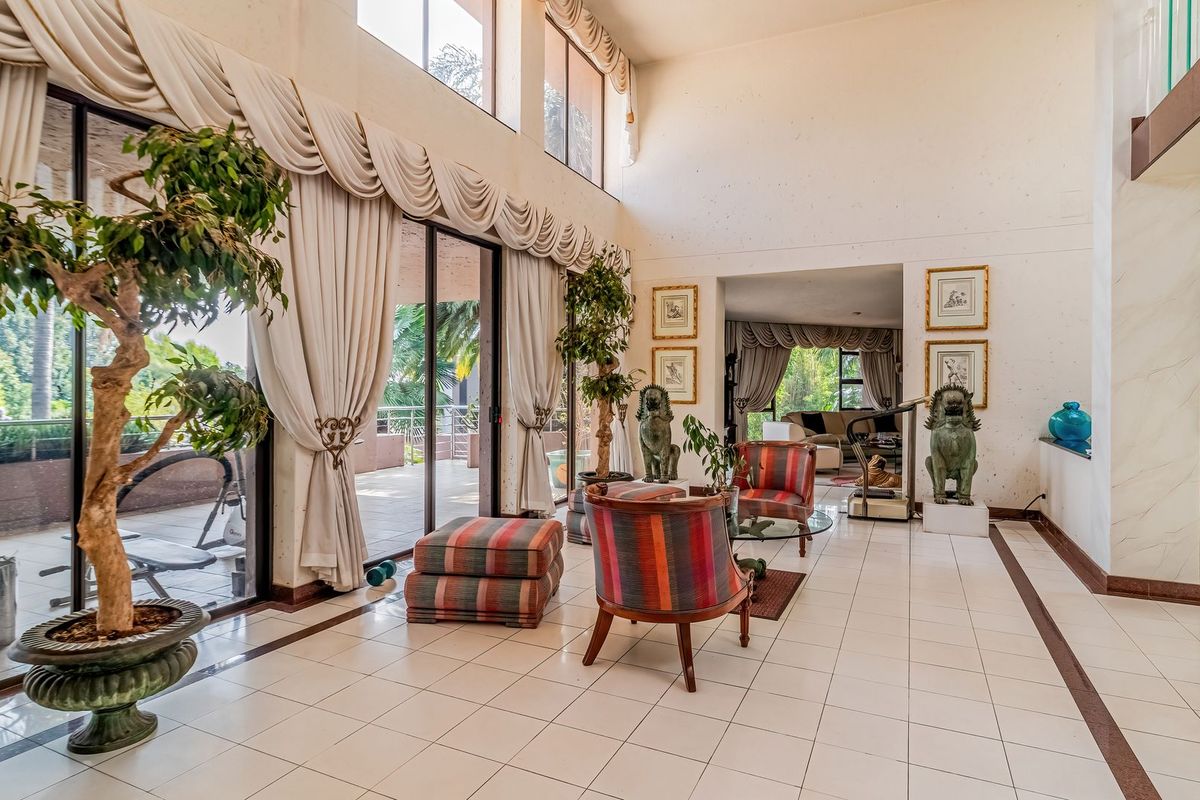 Spacious double-volume living area featuring large windows, tiled flooring, and direct access to an outdoor patio through sliding glass doors.