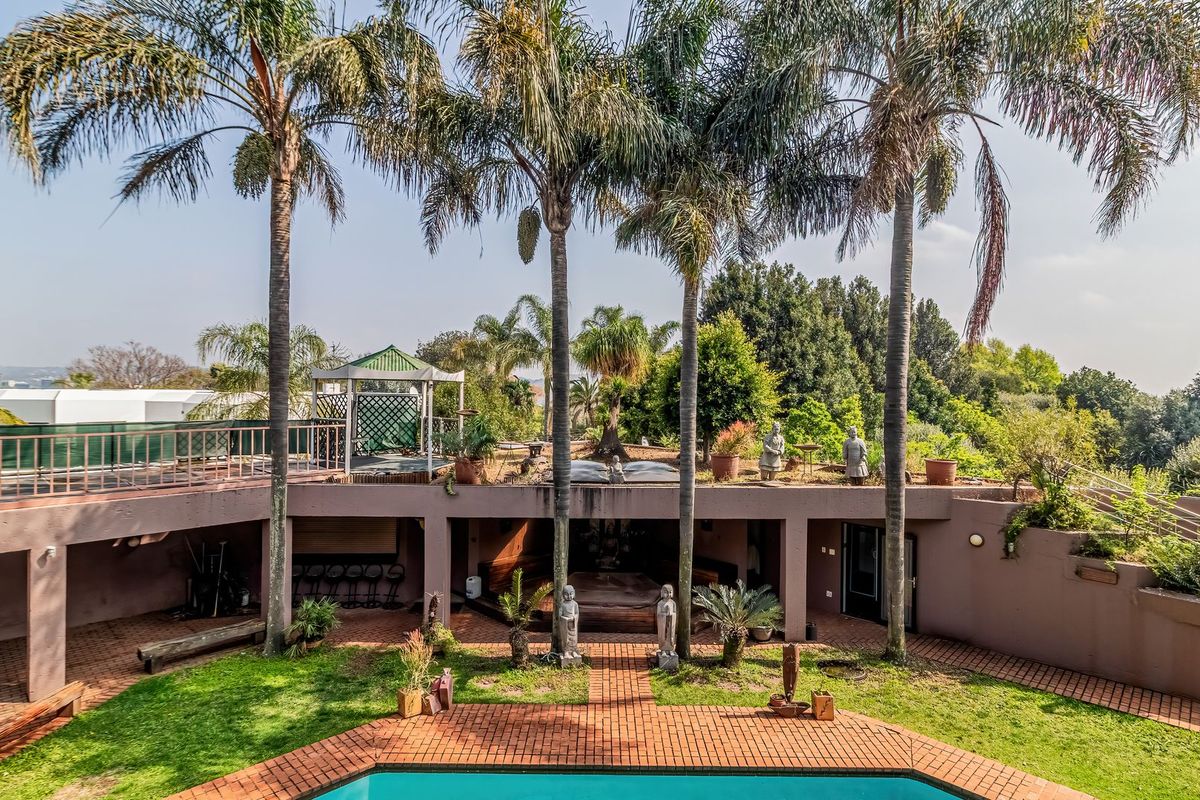 Spacious rear garden featuring a swimming pool, brick paved patio, mature palm trees, and a covered outdoor entertainment area with a built-in fireplace.