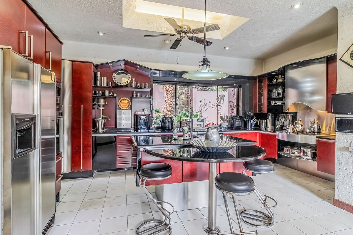 A spacious kitchen featuring dark red cabinetry, a central island with a breakfast bar, stainless steel appliances, and recessed ceiling lighting.