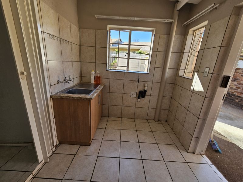 A functional laundry area featuring tiled walls and floors, a stainless steel sink with cabinetry, and dedicated plumbing connections for appliances.