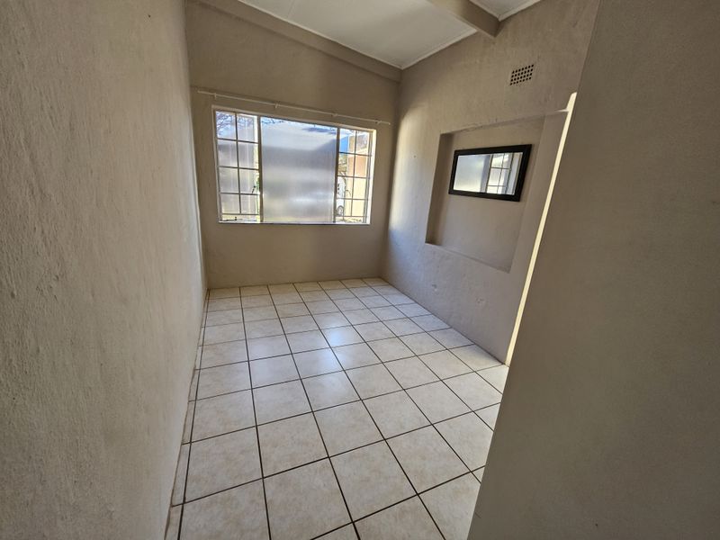 An empty bedroom featuring tiled flooring, a recessed wall niche, and a window, providing a blank canvas for personalization.