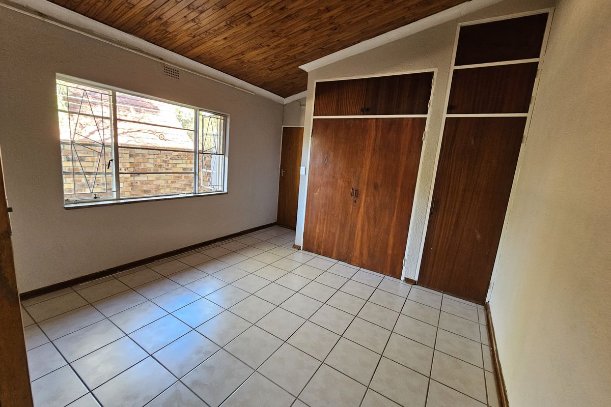 A vacant bedroom featuring tiled flooring, a wooden ceiling, and built-in wooden cupboards with overhead storage compartments.