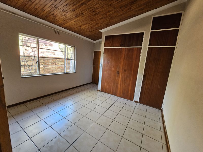 A vacant bedroom featuring tiled flooring, a wooden ceiling, and built-in wooden cupboards with overhead storage compartments.
