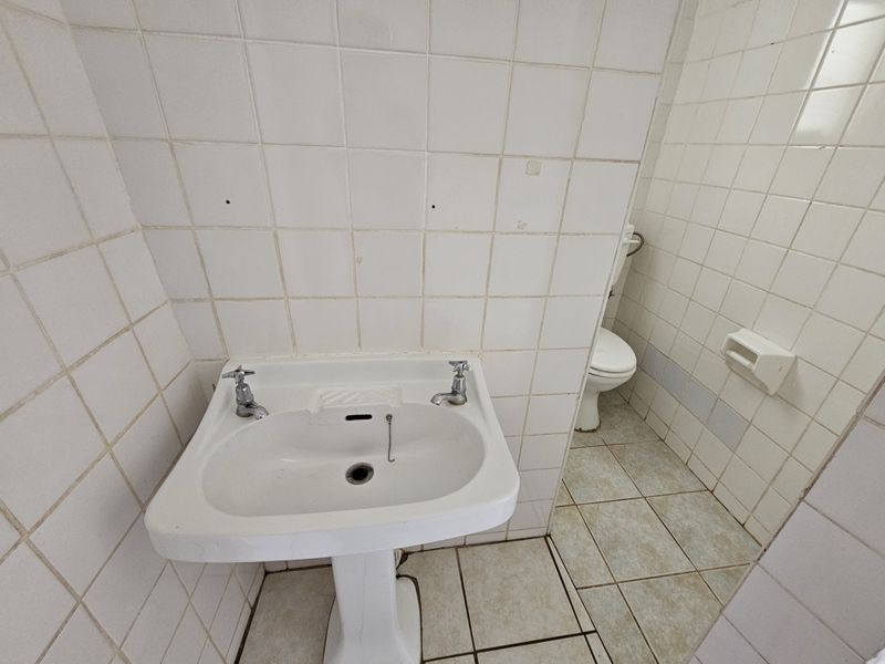 A dated bathroom featuring a pedestal basin and toilet with original ceramic wall and floor tiling, requiring modernization and cosmetic updates.