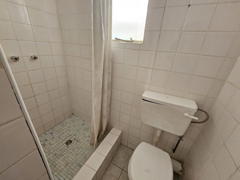 A compact bathroom featuring a shower enclosure and toilet with dated white wall tiling and floor finishes.