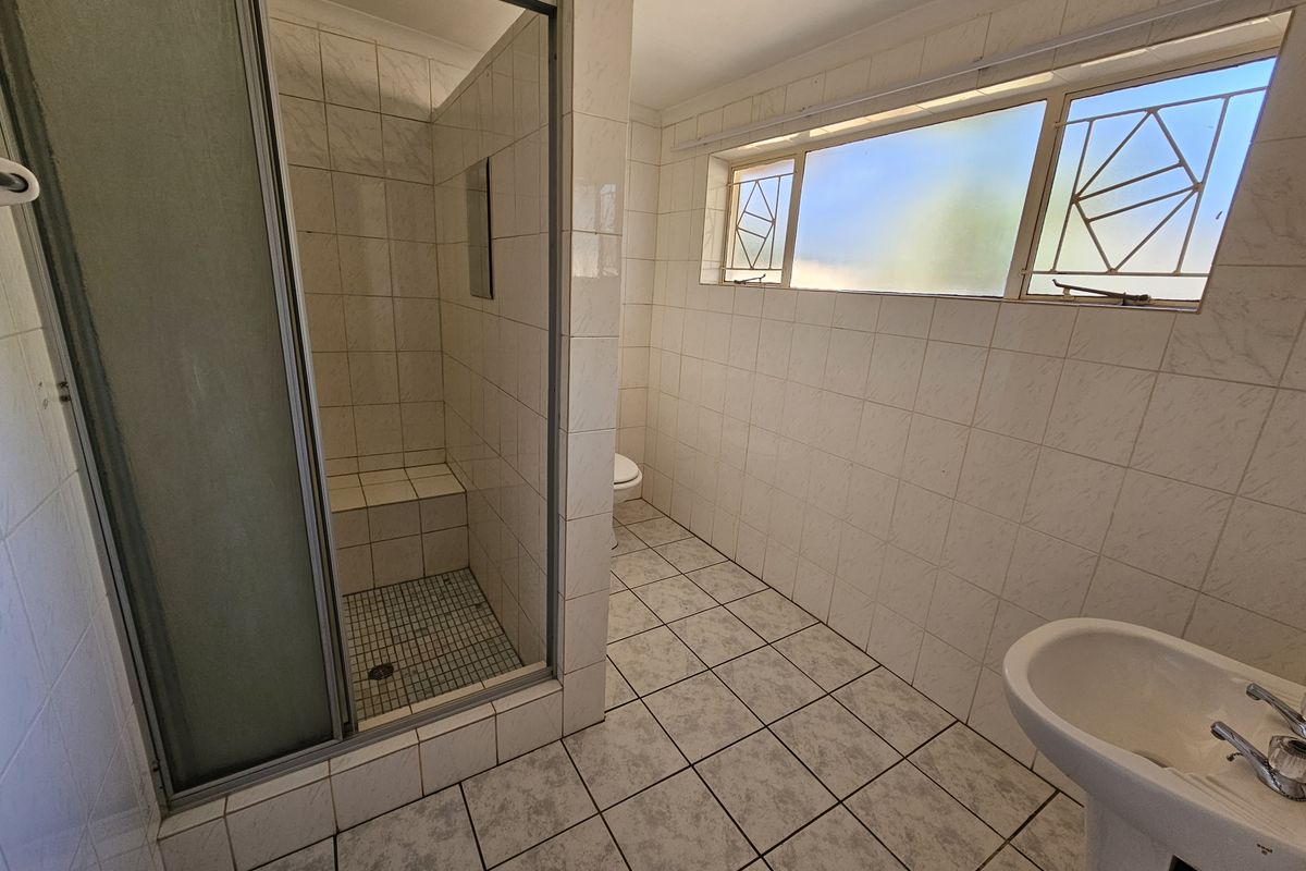 A functional bathroom featuring a shower enclosure, pedestal basin, and toilet, finished with tiled walls and flooring throughout.