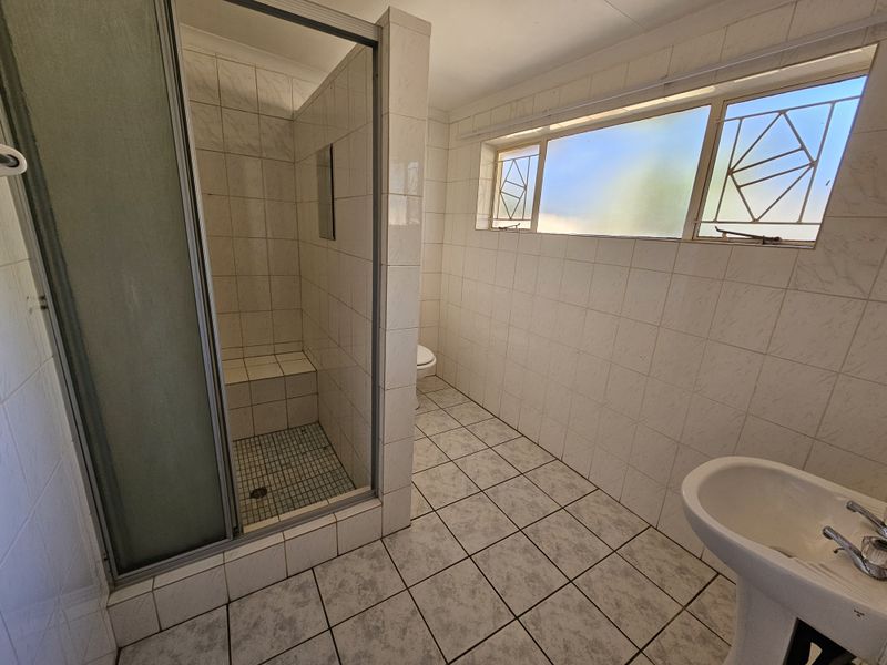 A functional bathroom featuring a shower enclosure, pedestal basin, and toilet, finished with tiled walls and flooring throughout.