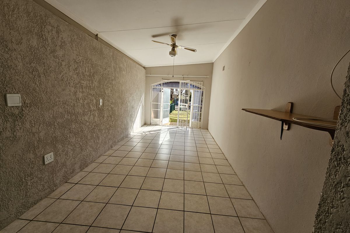 An empty, elongated living area featuring tiled flooring, a ceiling fan, and direct access to the garden through glass-paned french doors.