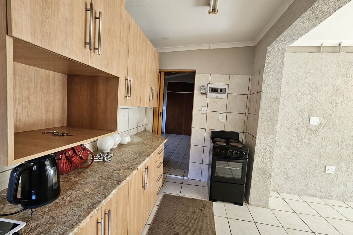 Functional kitchen featuring laminate cabinetry, stone-look countertops, and ceramic floor tiling, offering a practical layout with direct access to adjacent living areas.