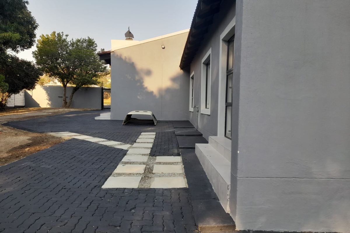 A view of the rear exterior featuring a paved driveway, concrete steps, and modern grey painted walls.