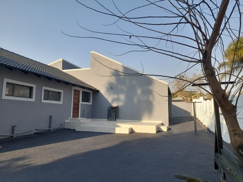 Rear exterior view of the house featuring a paved driveway, a raised concrete patio area, and a modern grey facade with tiled roofing.