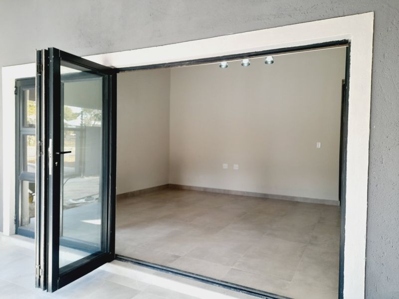 An empty, modern living area featuring large black bi-fold doors, neutral tiled flooring, and recessed ceiling spotlights.