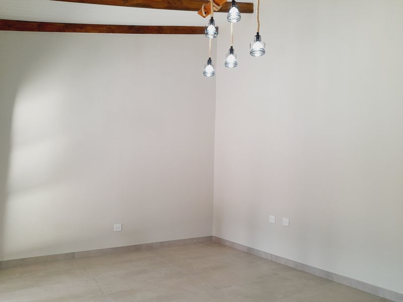 A bright, empty living space featuring neutral tiled floors, exposed timber ceiling beams, and a modern pendant light fixture.