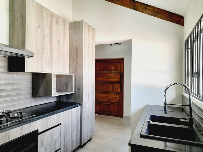 Modern kitchen featuring light wood-grain cabinetry, dark stone countertops, integrated gas hob, extractor fan, and a double sink with a contemporary gooseneck faucet.