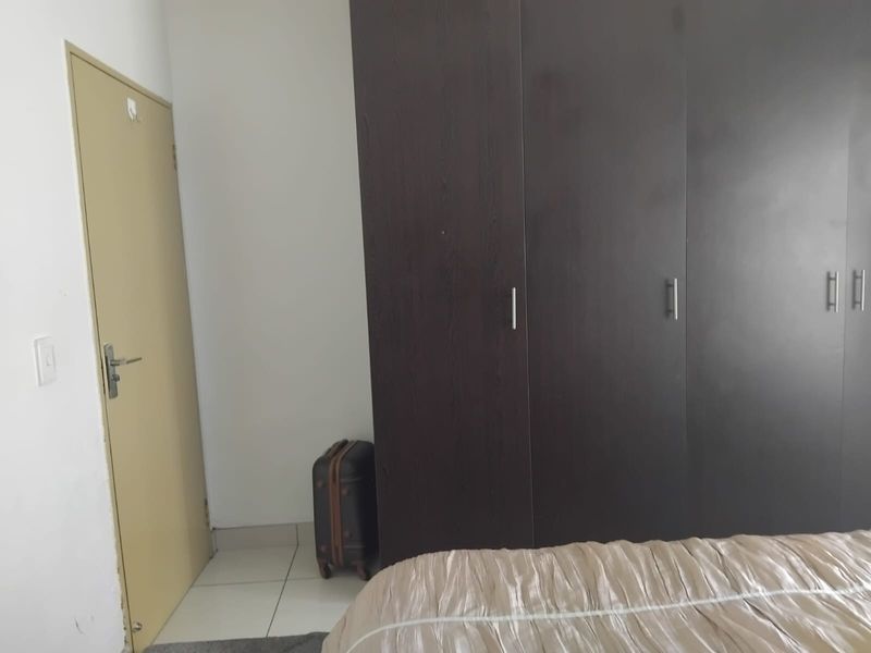 A bedroom featuring dark wood built-in cupboards and neutral tiled flooring.