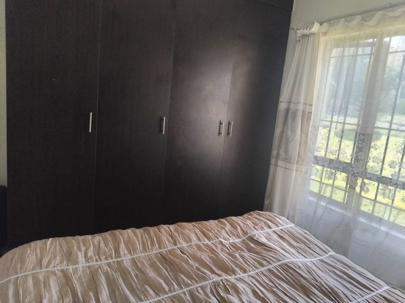 A bedroom featuring dark wood built-in cupboards and a window with natural light.