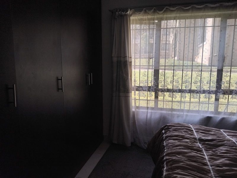 A bedroom featuring dark built-in cupboards and a window fitted with security bars, overlooking an outdoor area.