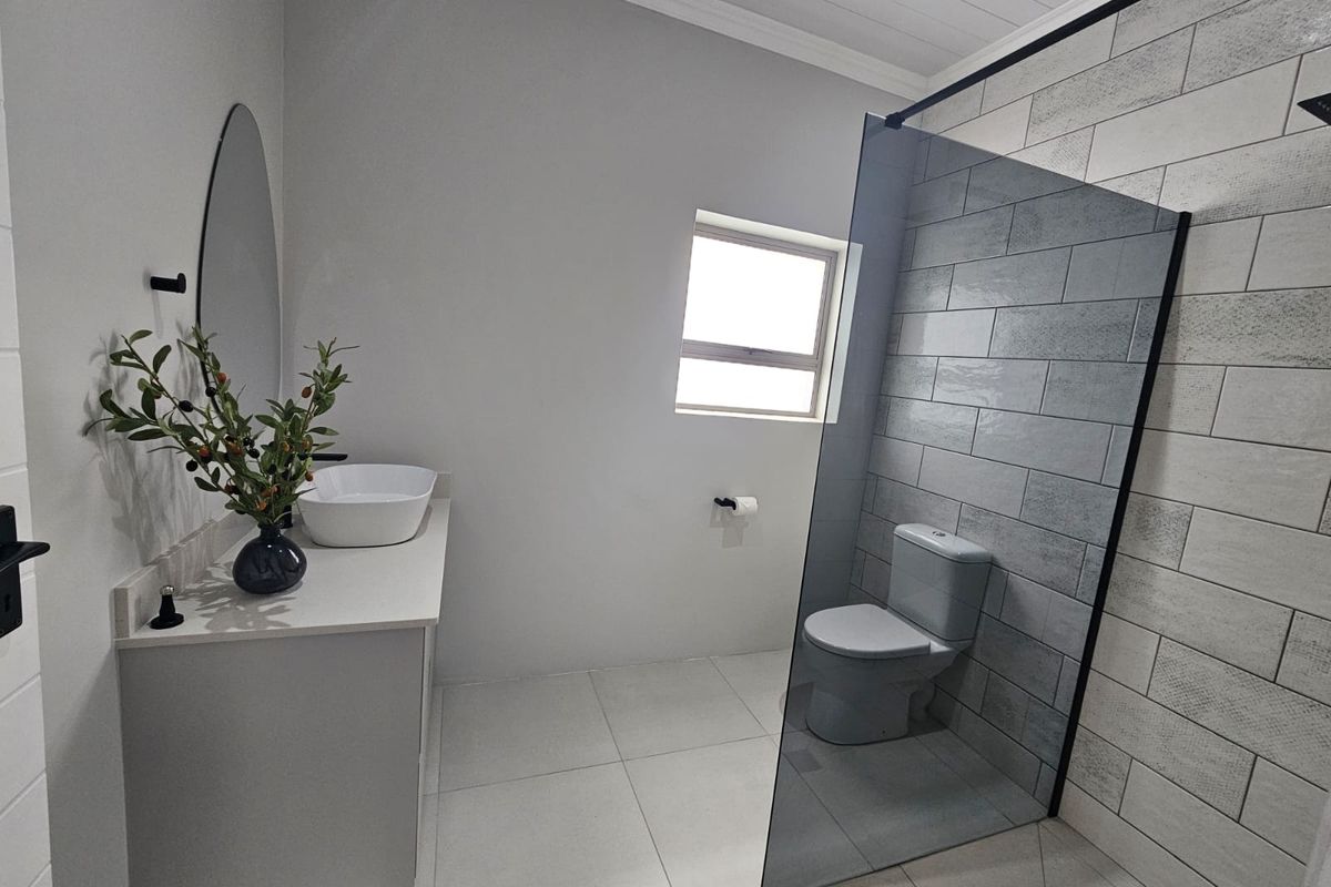 Modern bathroom featuring a sleek vanity with vessel sink, a glass-enclosed toilet area, and contemporary subway wall tiling.
