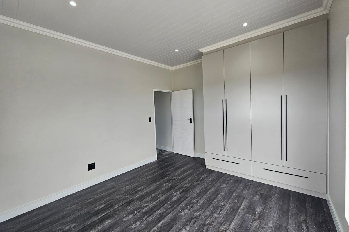 A clean, modern bedroom featuring neutral walls, dark laminate flooring, a tongue and groove ceiling with recessed lighting, and ample built-in cupboard space.
