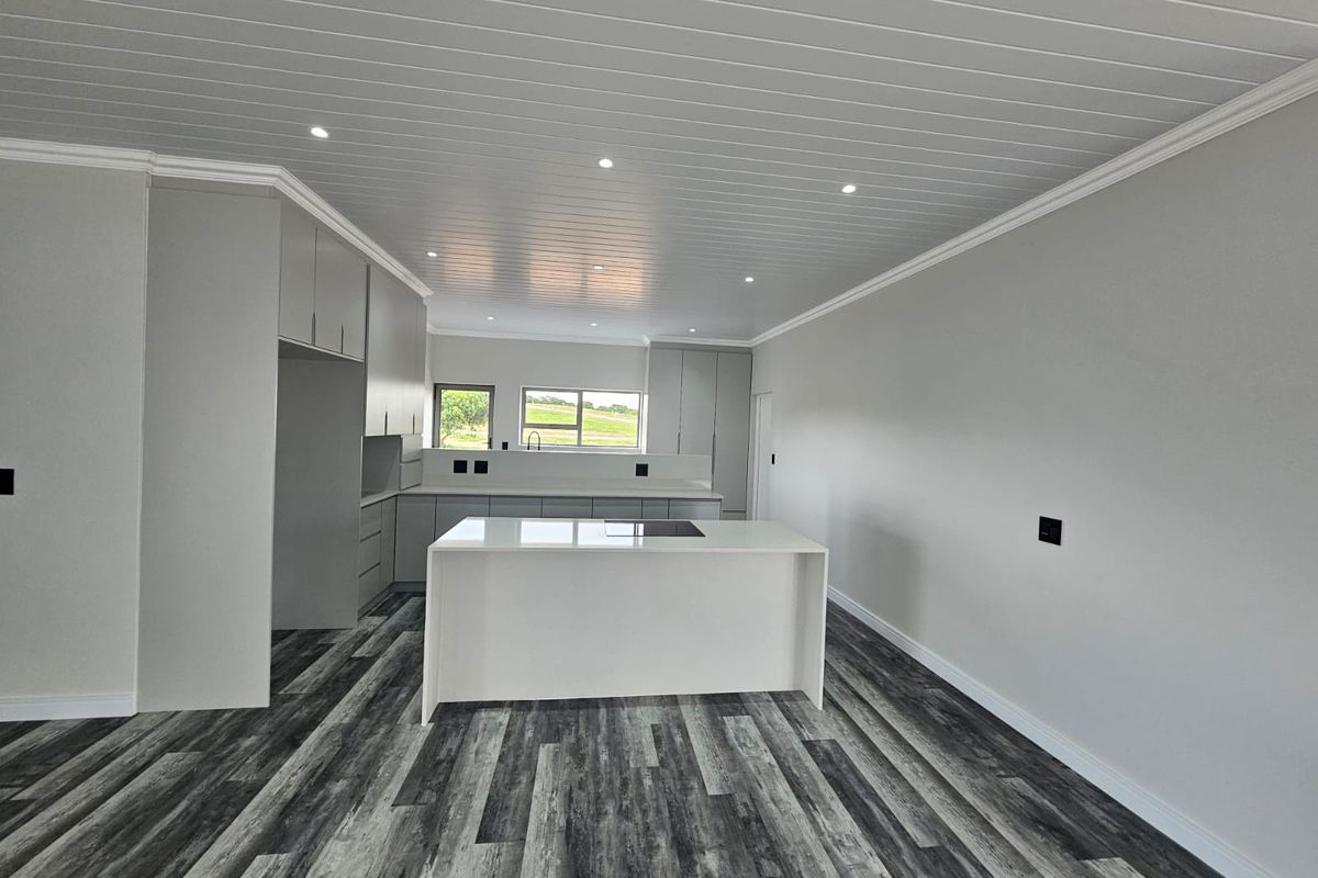 Modern, open-plan kitchen featuring a central island with a built-in cooktop, sleek cabinetry, and contemporary wood-look flooring under a clean tongue and groove ceiling.
