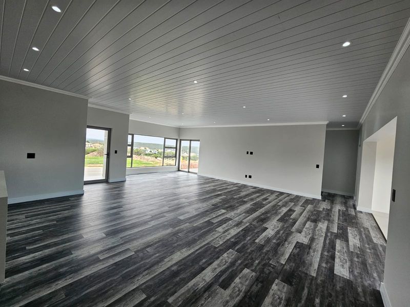 Spacious open-plan living area featuring modern laminate flooring, a clean tongue and groove ceiling with recessed lighting, and large windows with exterior views.