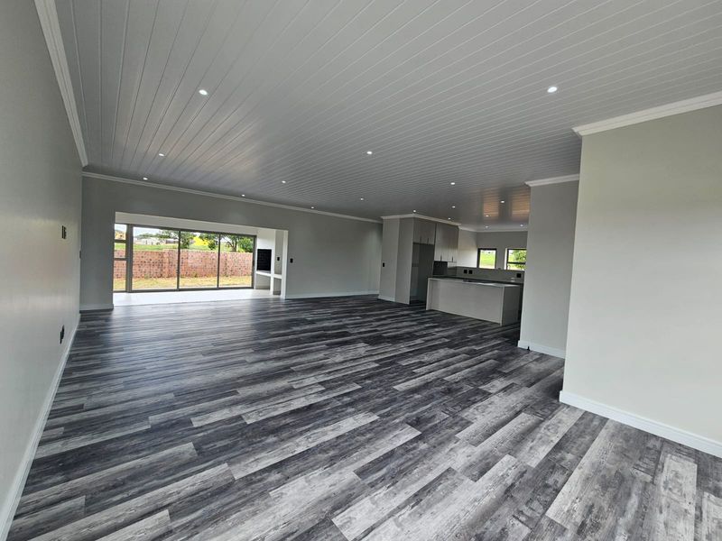 Spacious open-plan living and kitchen area featuring modern laminate flooring, recessed downlights, tongue and groove ceilings, and seamless access to the outdoor patio.
