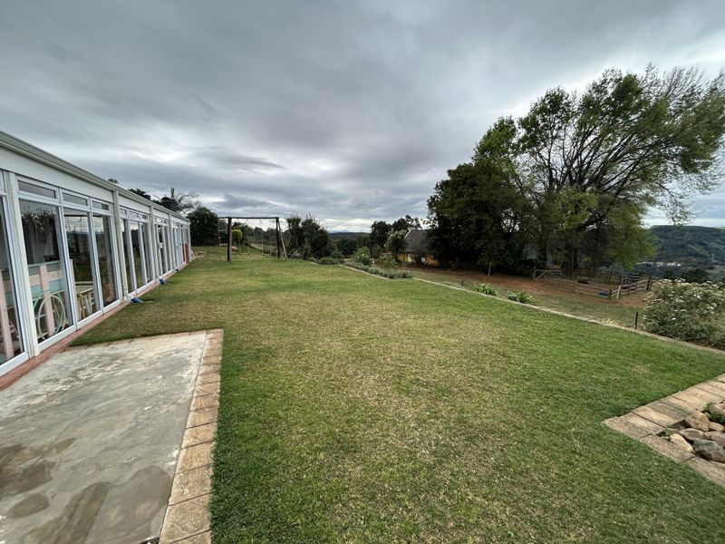 Spacious rear garden featuring a large lawn, paved patio area, and an enclosed sunroom with extensive glass sliding doors.